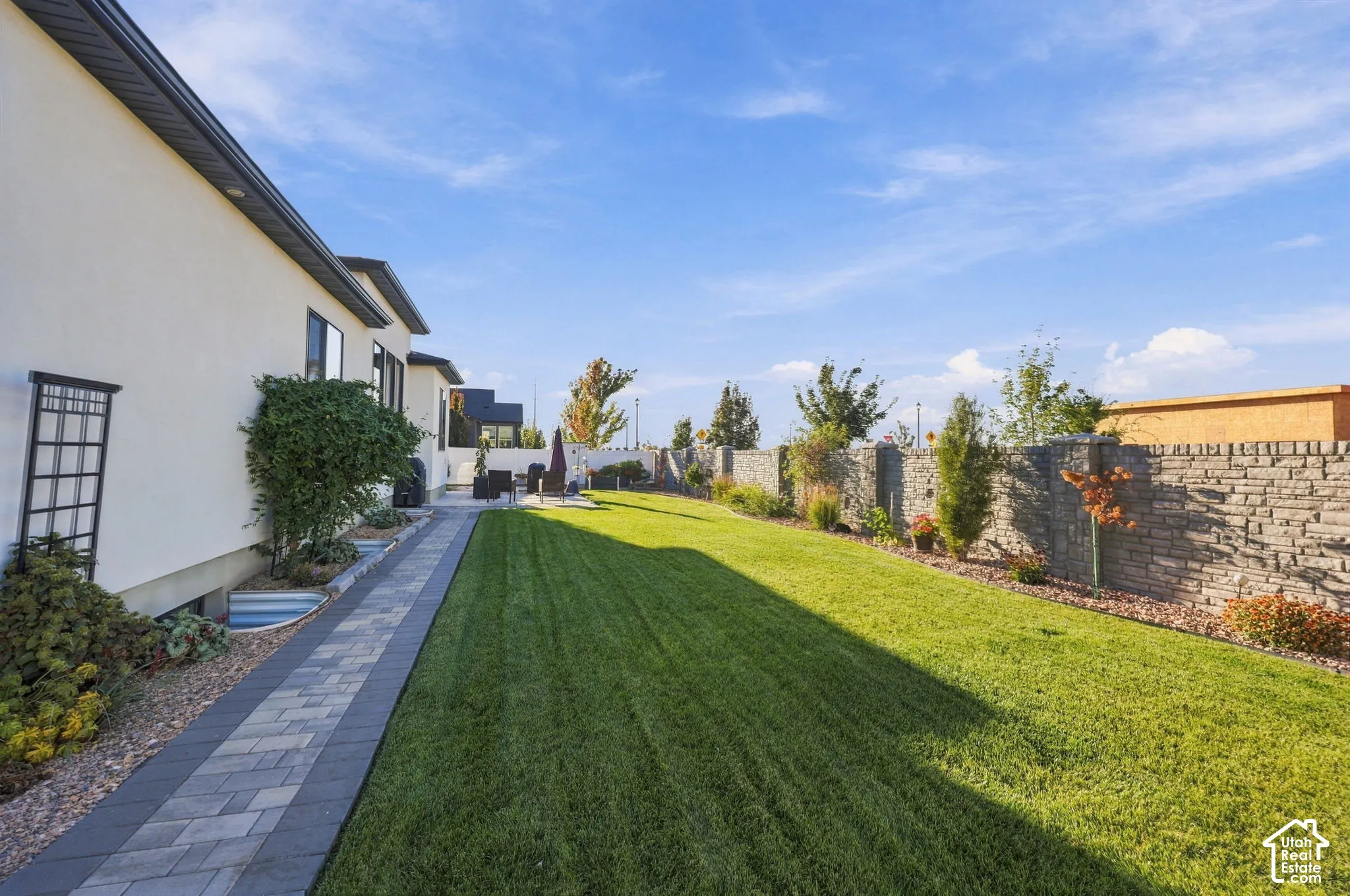 Expansive backyard featuring a manicured lawn, paver patio, and stone retaining wall