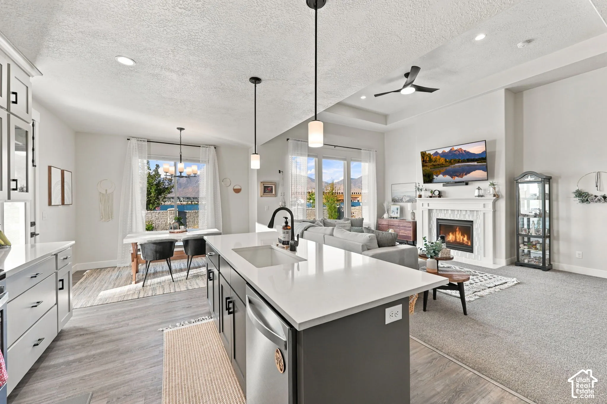 Open-concept living space featuring a kitchen island with sink, a dining area with pendant lighting, and a living area with a built-in fireplace
