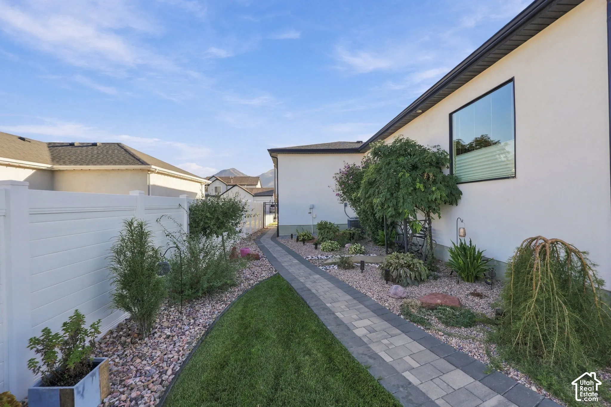 White stucco exterior with a large picture window, paver pathway, decorative rock landscaping, and a white privacy fence