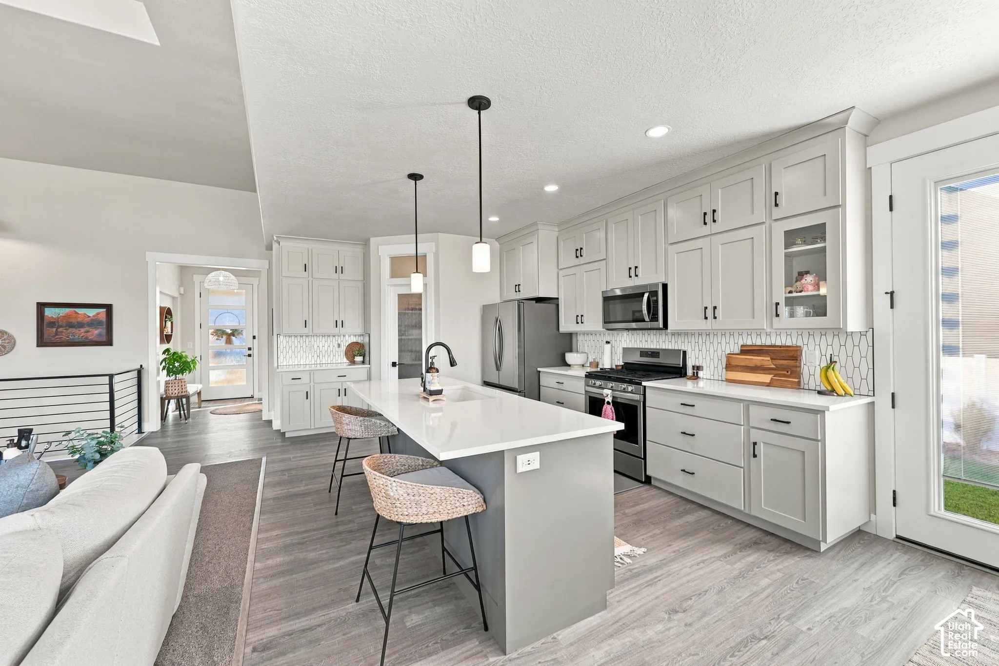 Kitchen featuring light gray cabinetry, stainless steel appliances, a white tile backsplash, a central island with a white countertop, and wood-finish flooring
