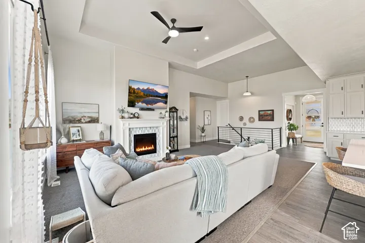 Recessed ceiling with an integrated fan, custom fireplace featuring a tile surround and mantel, and wood-finish flooring