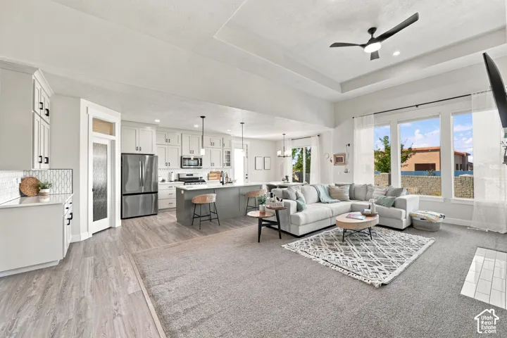 Open-concept living space featuring a spacious kitchen, built-in stainless steel appliances, large windows, and a tray ceiling with a modern ceiling fan