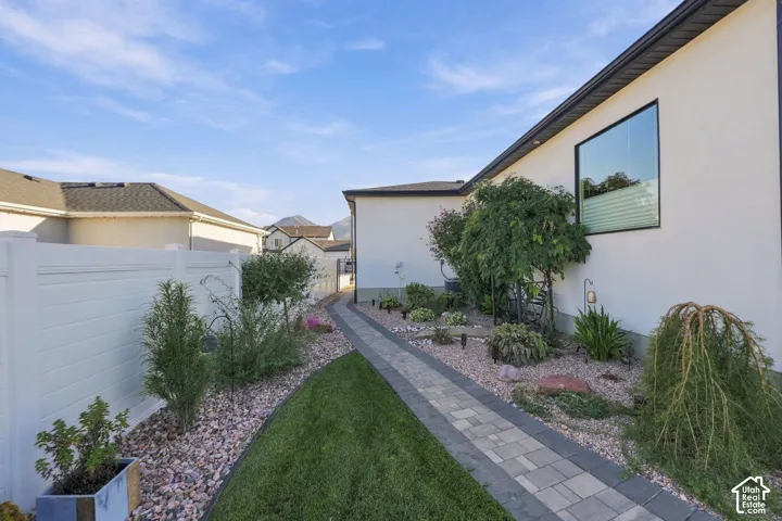 White stucco exterior with a large picture window, paver pathway, decorative rock landscaping, and a white privacy fence