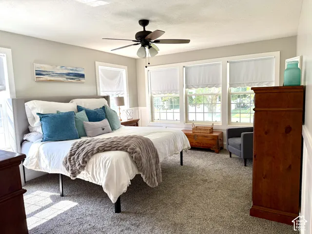 Carpeted flooring, multiple windows, ceiling fan with light, and wainscoting details