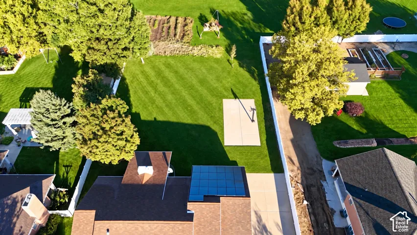 Expansive green lawn, mature trees, concrete patio, solar panels, and white privacy fencing