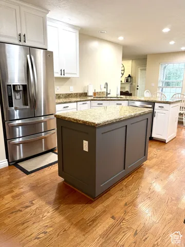 Kitchen featuring a stainless steel refrigerator, white cabinetry, granite countertops, and wood-finish flooring