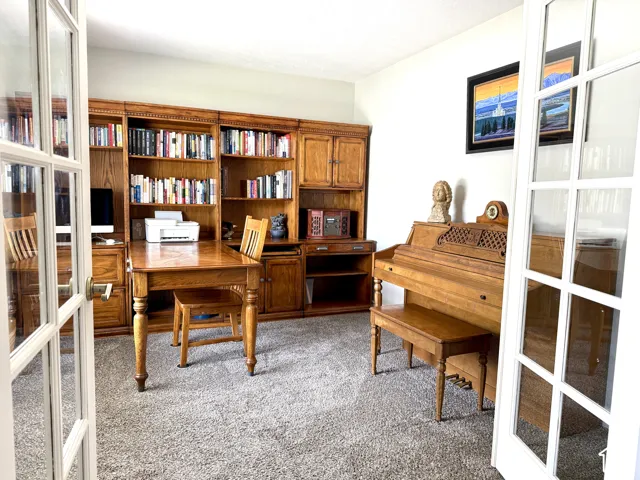 French doors opening into a room featuring extensive built-in wood cabinetry and shelving, with wall-to-wall carpeting