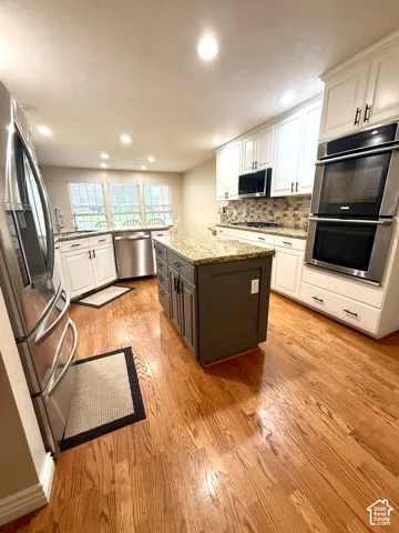 Kitchen featuring wood-finish flooring, two-tone cabinetry, stainless steel appliances, a center island with a stone-finish countertop, and recessed lighting