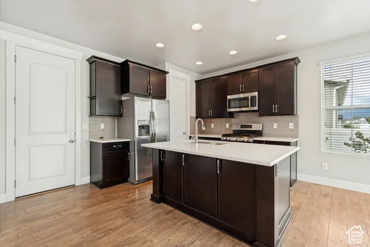 Kitchen featuring dark wood cabinetry, a central island with a light-toned countertop, stainless steel appliances, wood-finish flooring, and recessed lighting