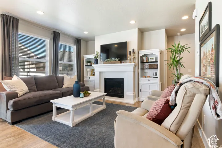 Recessed lighting throughout, a built-in fireplace with a white mantel, and wood-finish flooring
