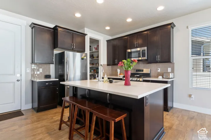 Kitchen featuring dark wood-finish cabinetry, stainless steel appliances, a spacious center island with a light-toned countertop, and wood-finish flooring