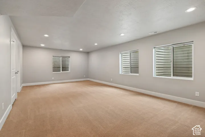 Expansive room featuring recessed lighting, three windows with blinds, and neutral tone carpeting