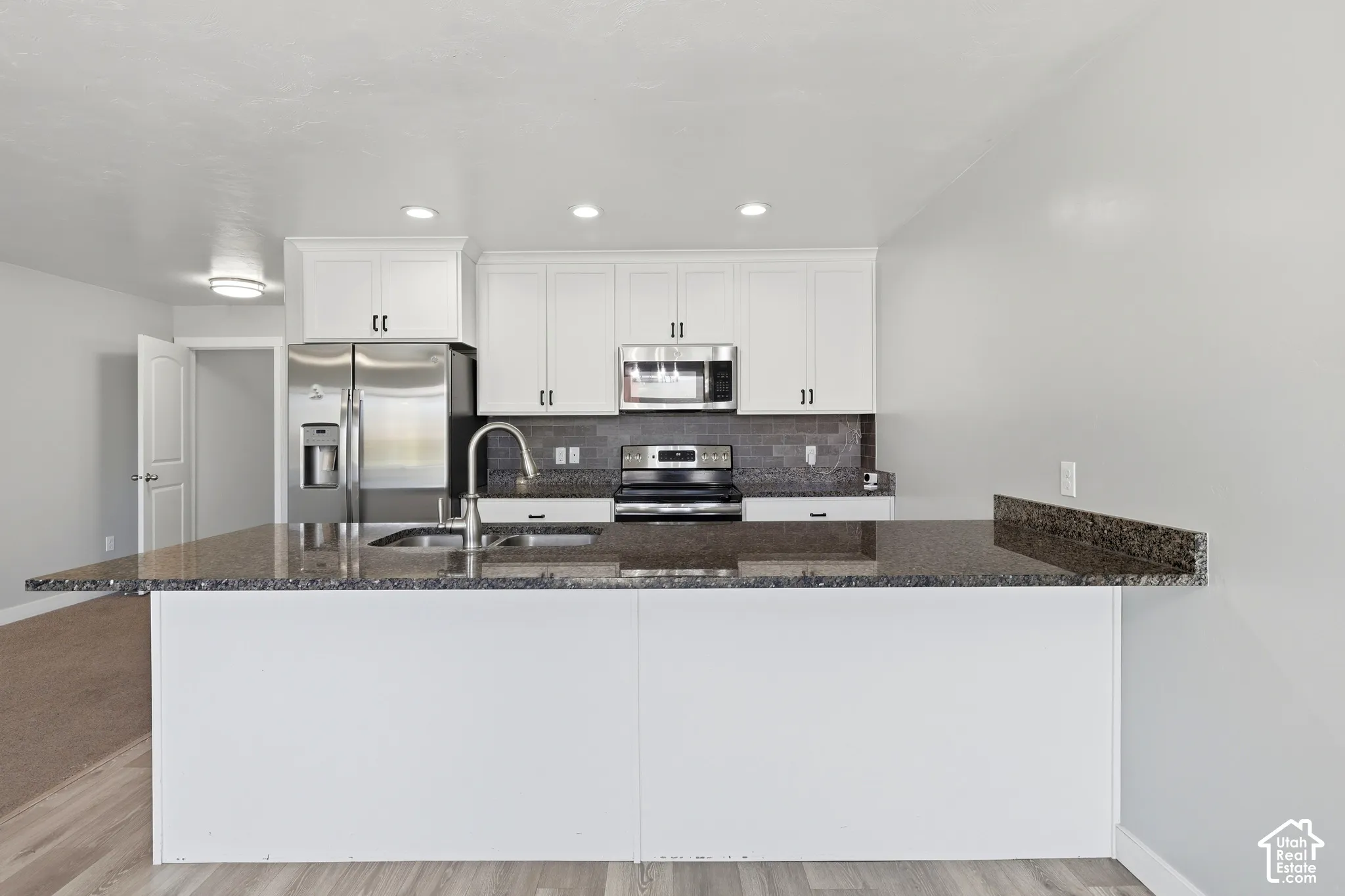 Kitchen featuring white cabinetry, stainless steel appliances, dark granite countertops, a tile backsplash, and recessed lighting