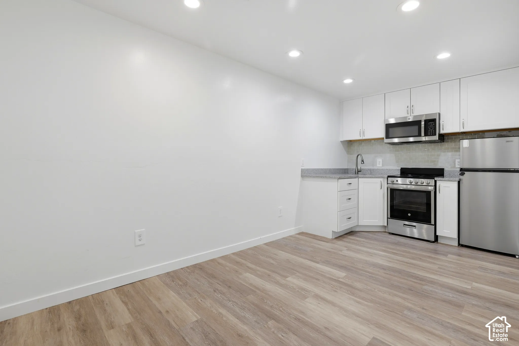 Recessed lighting illuminates the space featuring wood-finish flooring, white cabinetry, stainless steel appliances, and a tiled backsplash