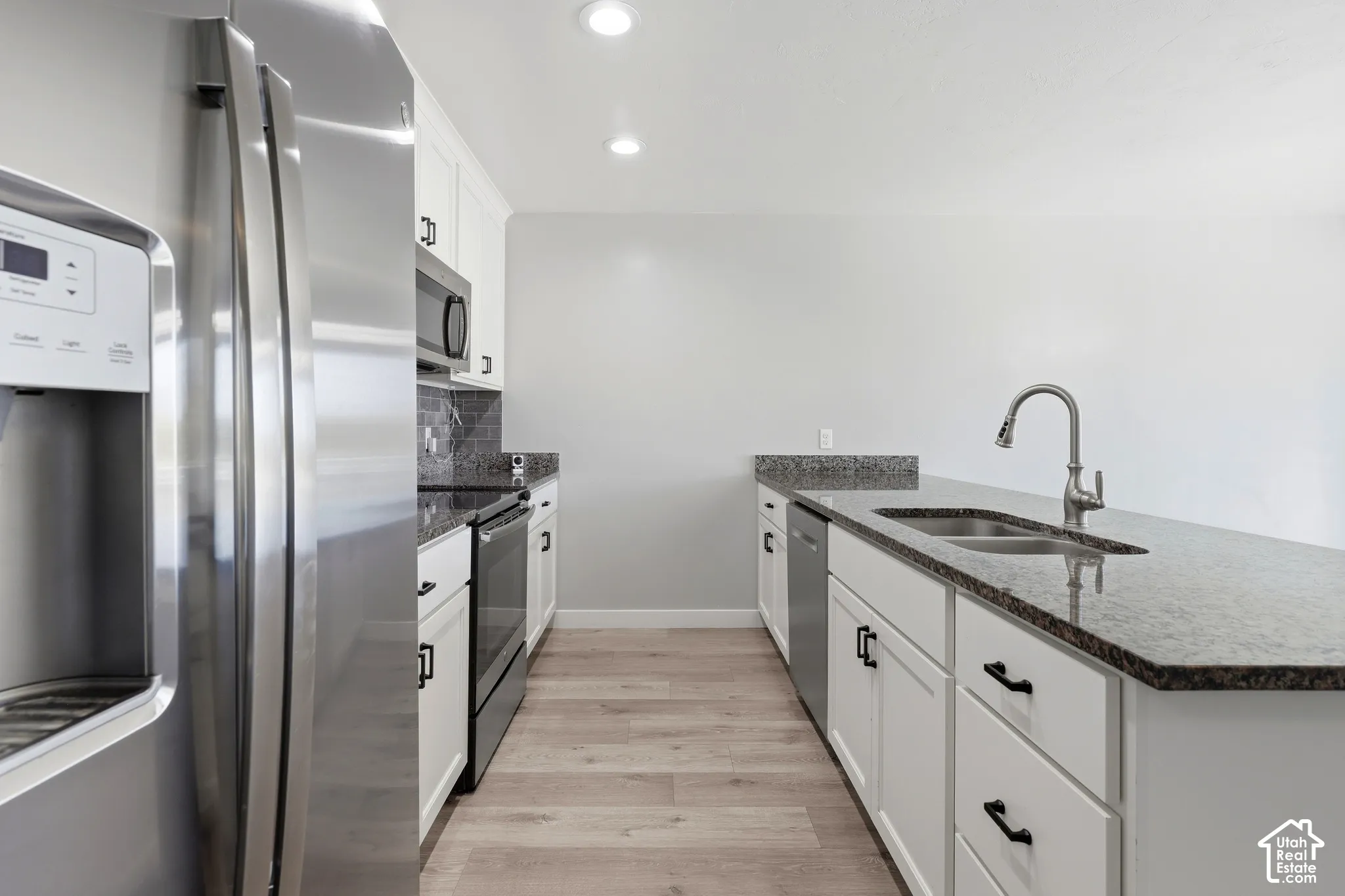 Kitchen featuring white cabinetry, dark stone countertops, stainless steel appliances, wood-finish flooring, and recessed lighting
