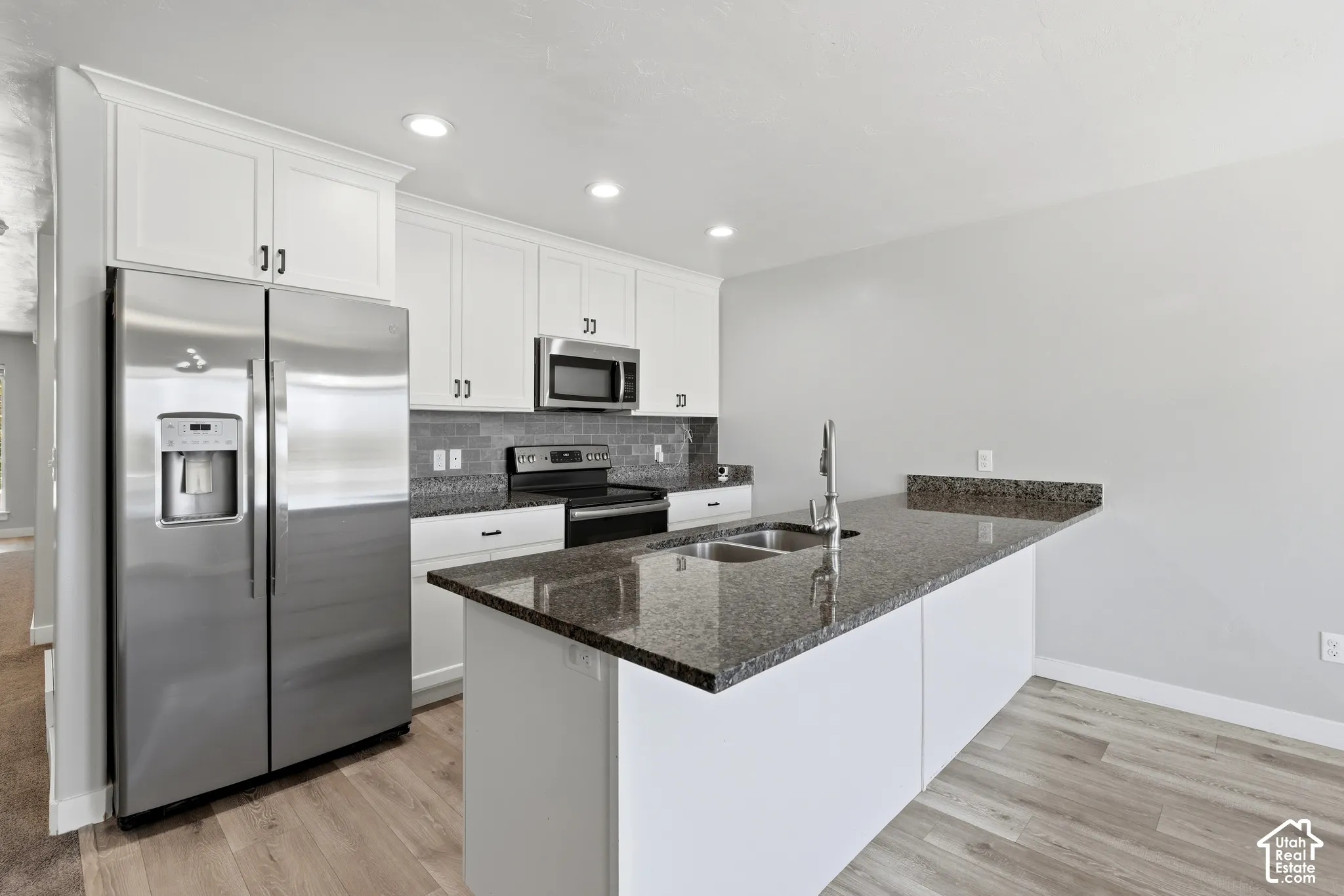 Kitchen featuring white cabinetry, dark stone countertops, stainless steel appliances, a double basin sink, and wood-finish flooring