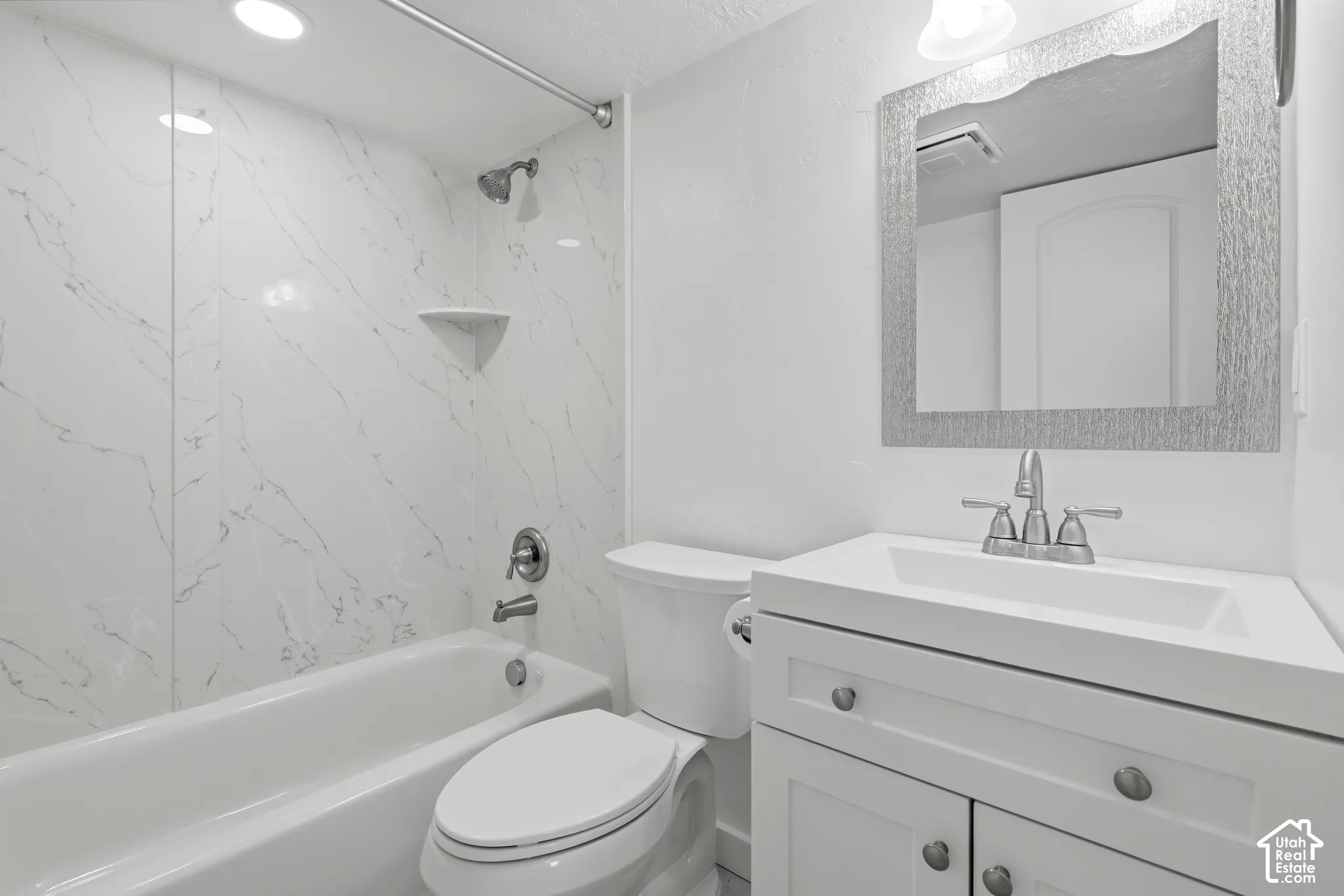 White vanity with an integrated sink and brushed nickel hardware, framed mirror, and a white bathtub with a tile surround
