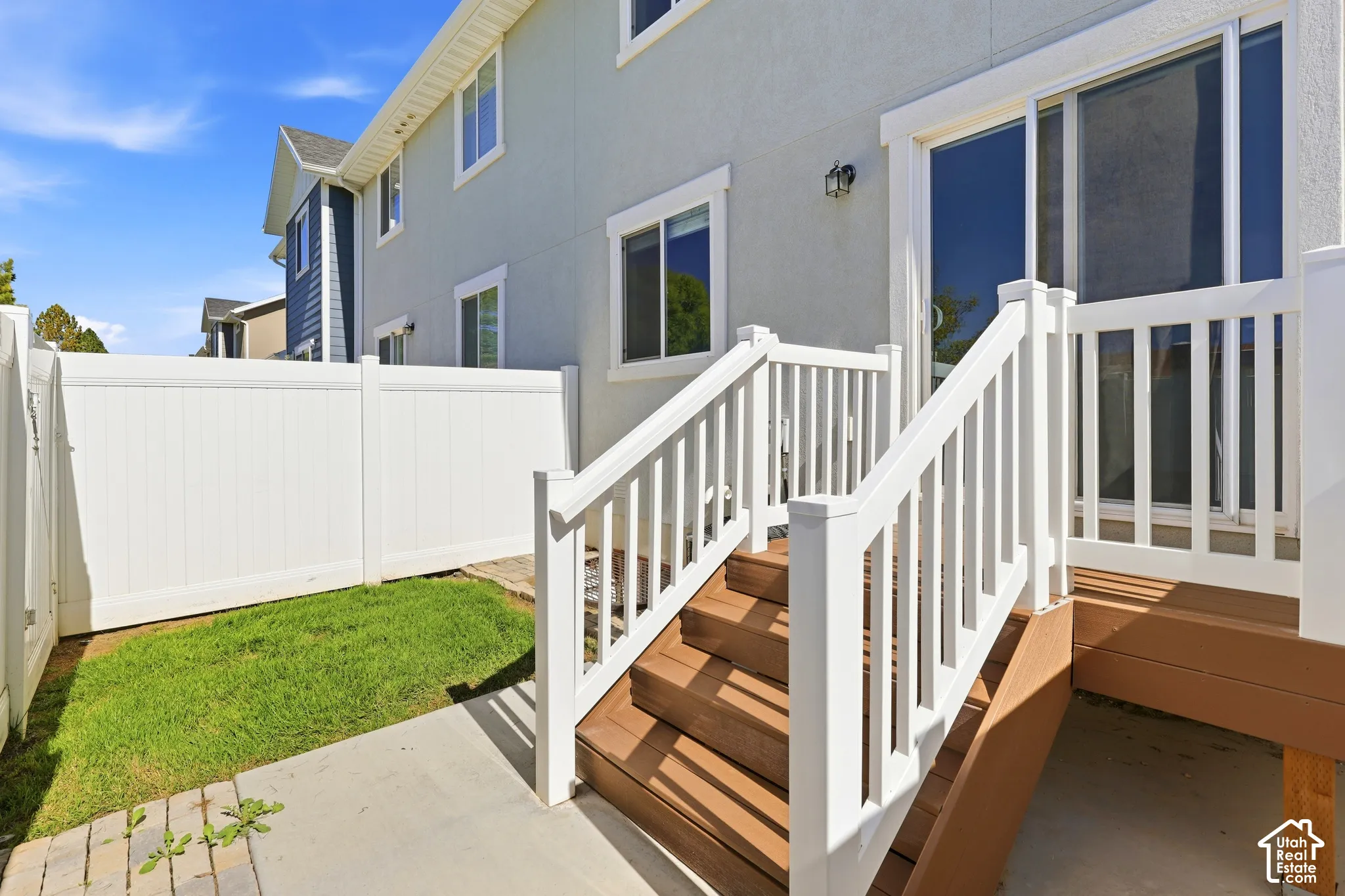 Private fenced yard with a composite wood deck and white railing, featuring a sliding glass door and exterior wall lighting