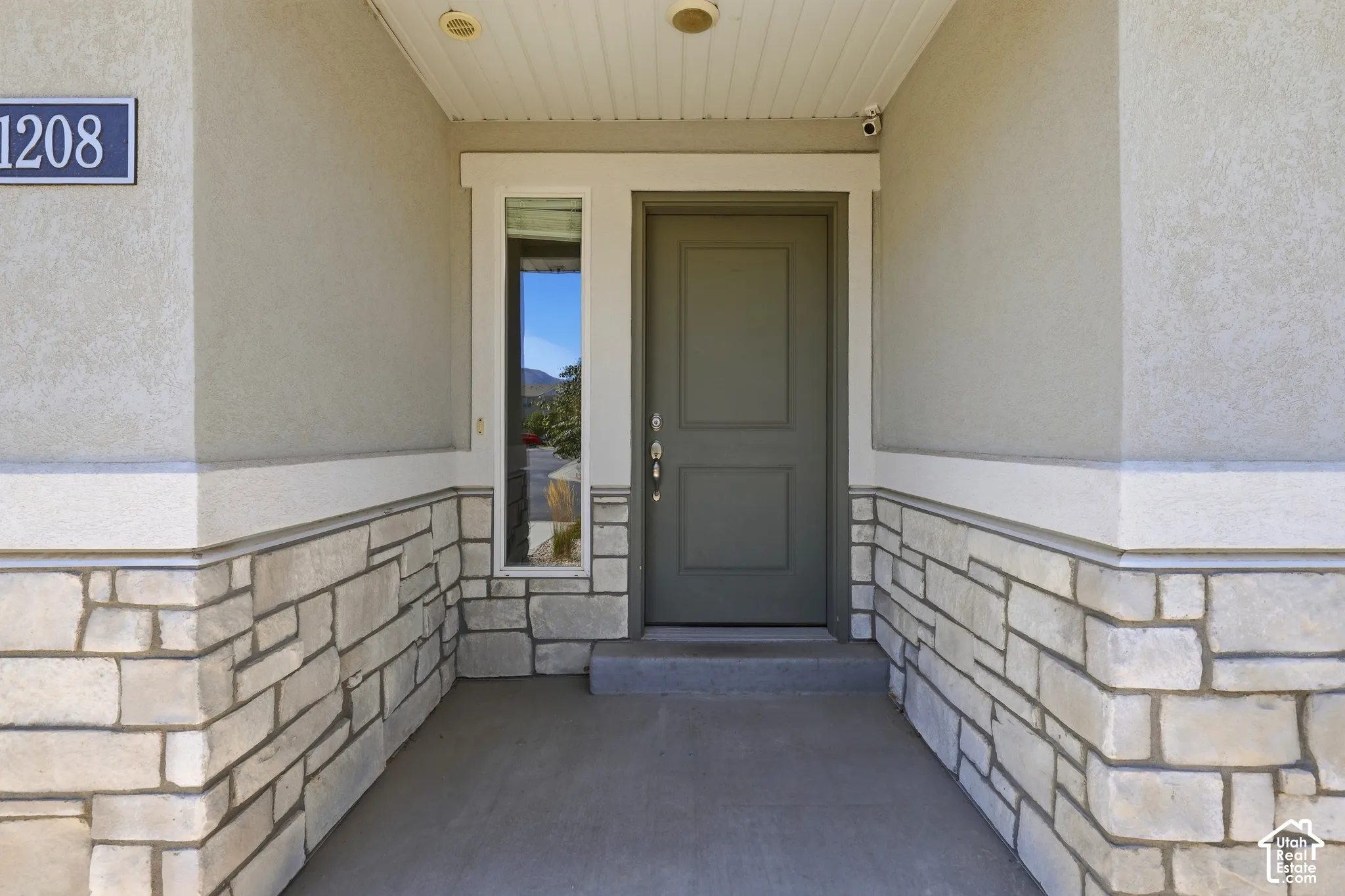 Entryway featuring stone veneer wainscoting, stucco siding, and a solid panel door with a sidelight