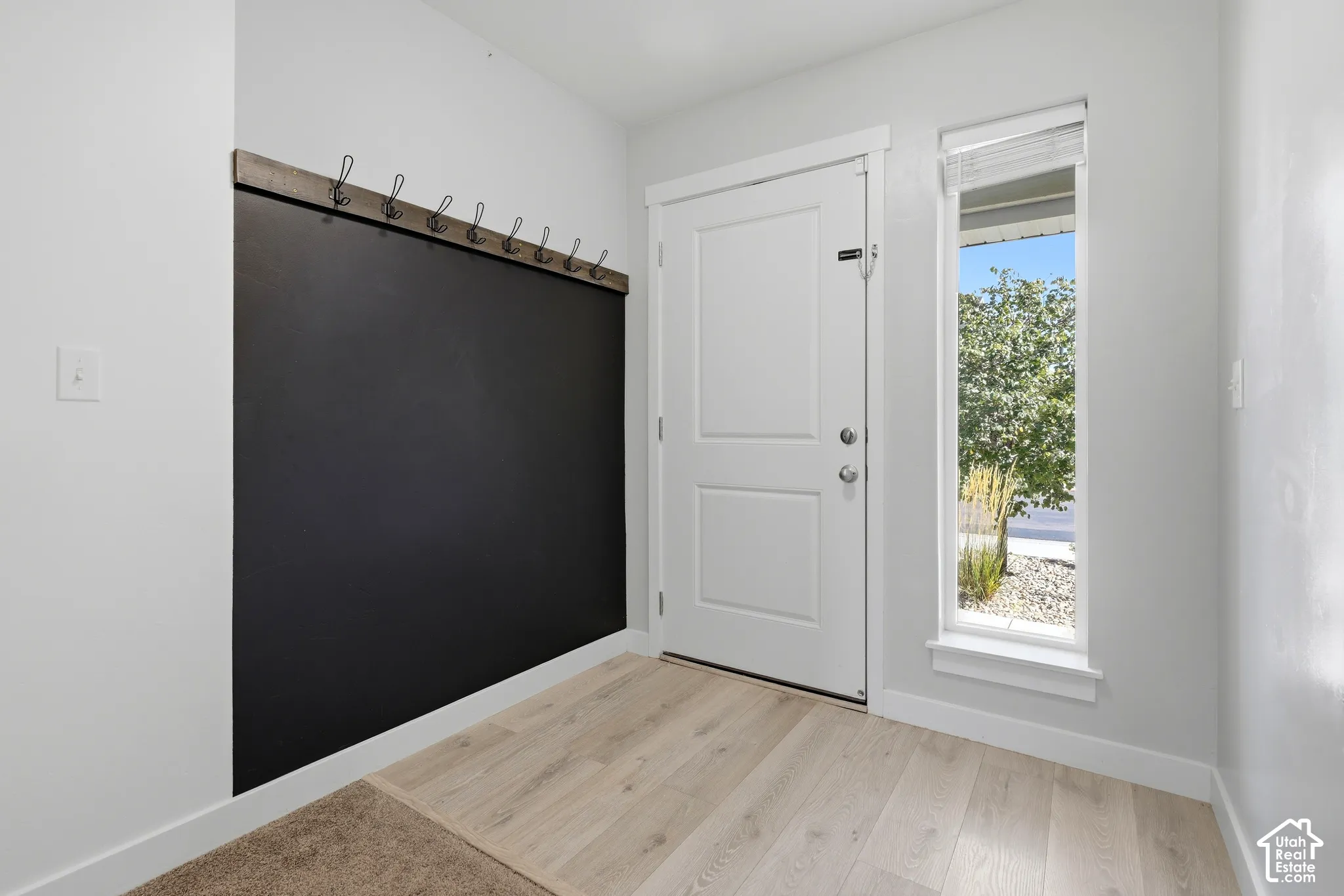 Entryway featuring wood-finish flooring, a full-lite door with a side window, and a built-in chalkboard wall with coat hooks