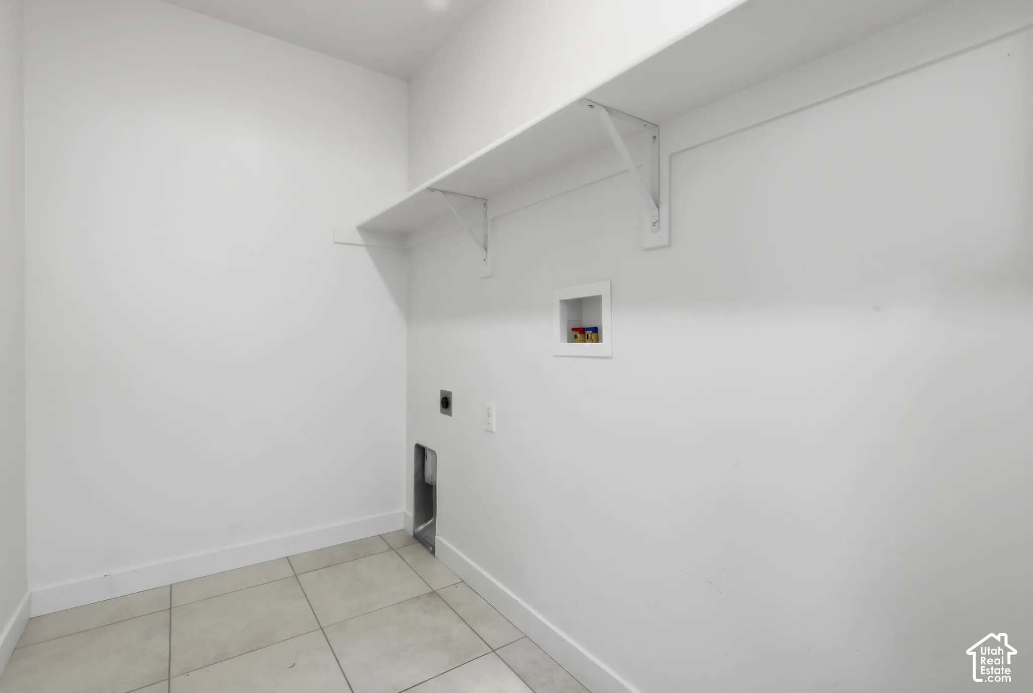 Utility area featuring tile flooring, a wall-mounted shelf, and appliance connections
