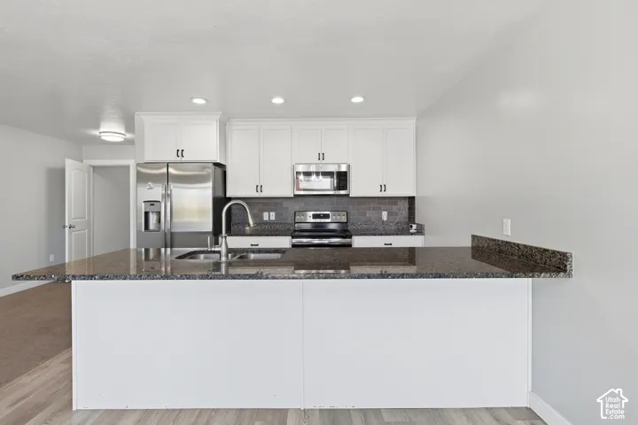 Kitchen featuring white cabinetry, stainless steel appliances, dark granite countertops, a tile backsplash, and recessed lighting