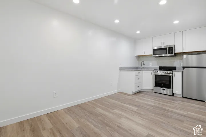 Recessed lighting illuminates the space featuring wood-finish flooring, white cabinetry, stainless steel appliances, and a tiled backsplash