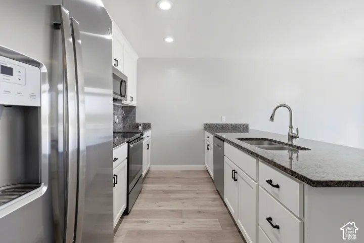 Kitchen featuring white cabinetry, dark stone countertops, stainless steel appliances, wood-finish flooring, and recessed lighting