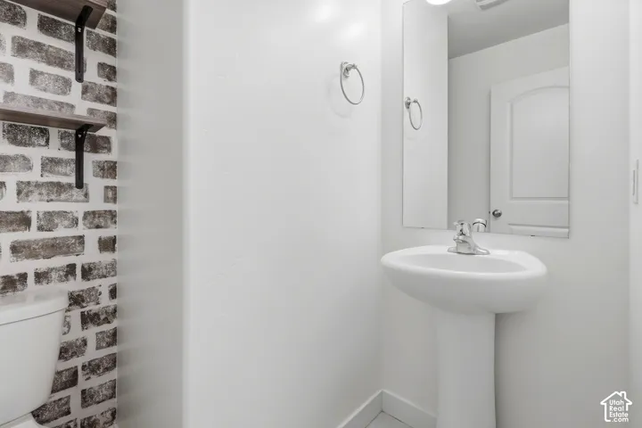 Pedestal sink with chrome faucet, wall-mounted mirror, and decorative brick-patterned wall