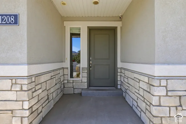 Entryway featuring stone veneer wainscoting, stucco siding, and a solid panel door with a sidelight