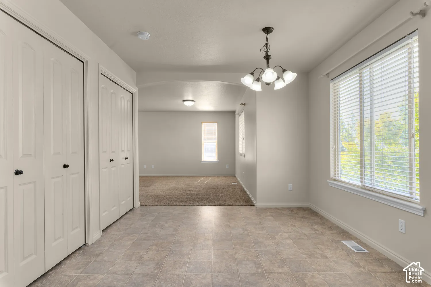 Neutral-toned interior with tile flooring, dual bi-fold closet doors, and a multi-bulb chandelier