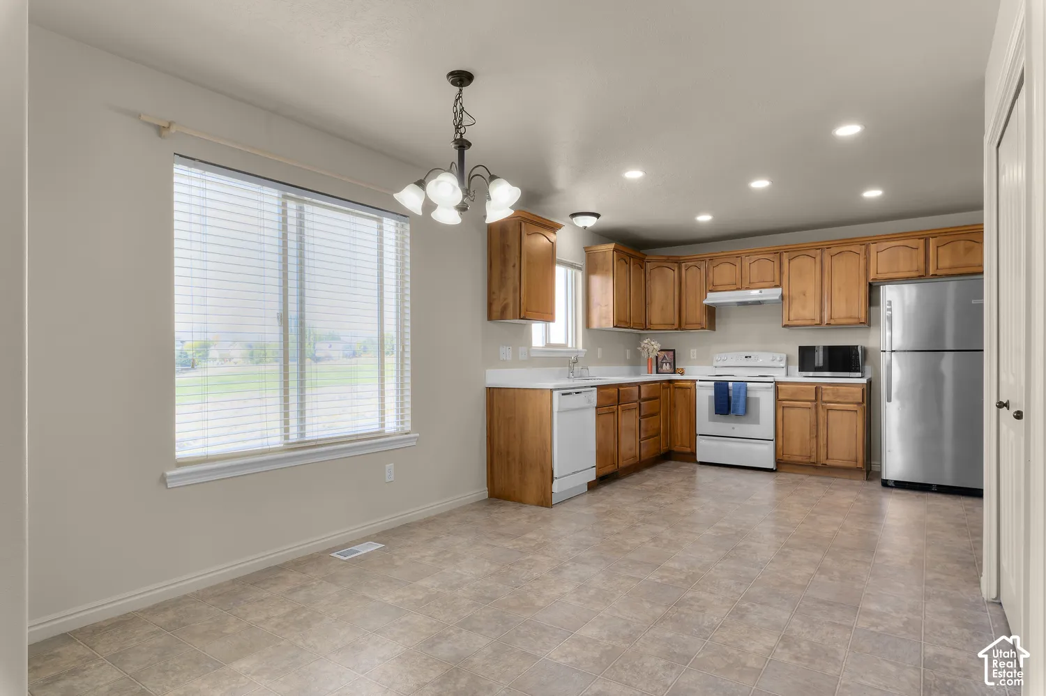 L-shaped kitchen with wood-finish cabinetry, white appliances, and recessed lighting