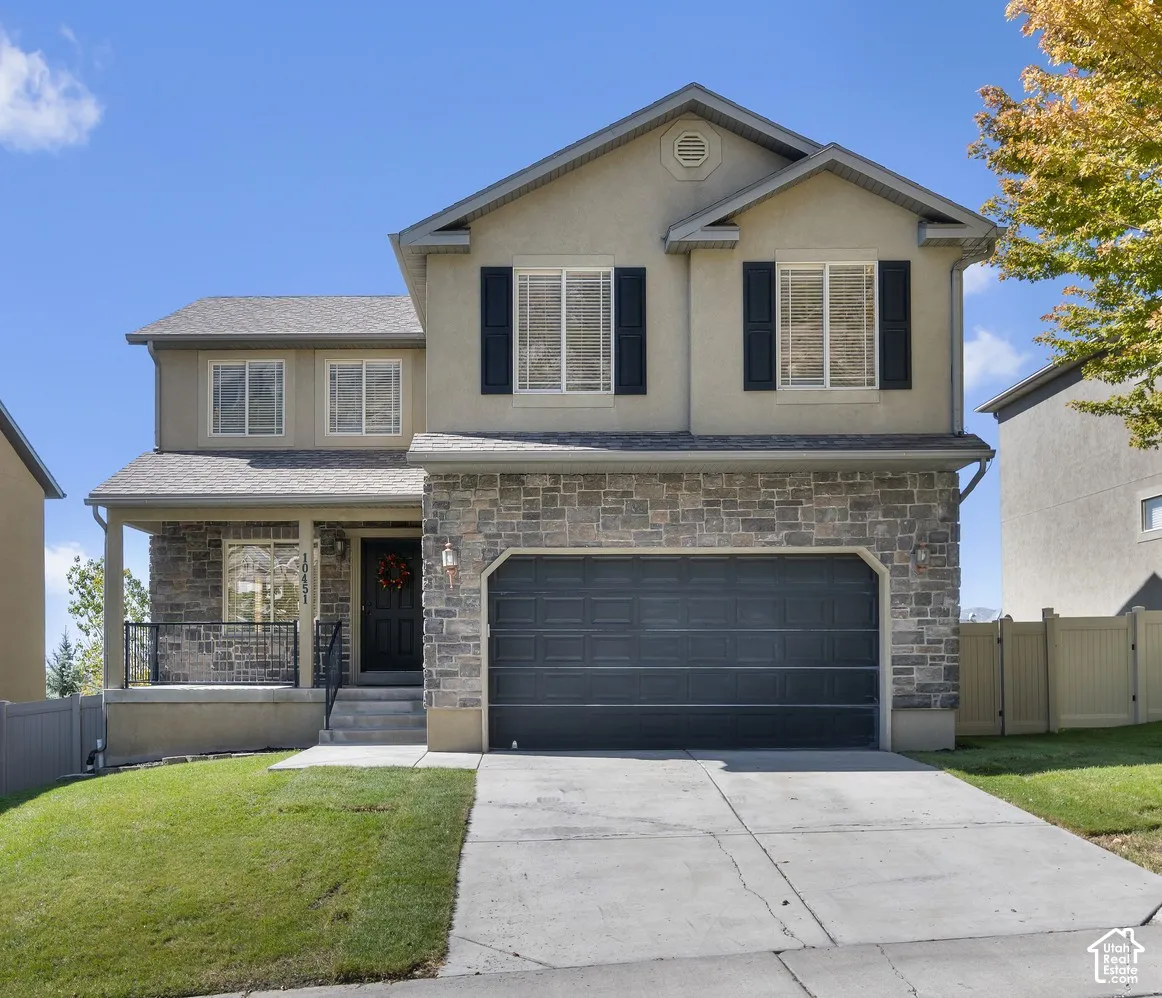 Two-story residence featuring a stone and stucco exterior, an attached two-car garage, and a covered front porch with railings