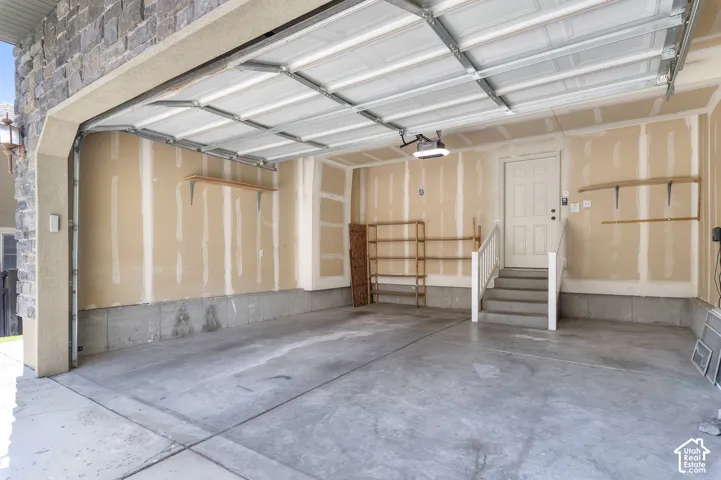 Attached garage with concrete flooring, automatic garage door opener, built-in shelving, and direct entry door