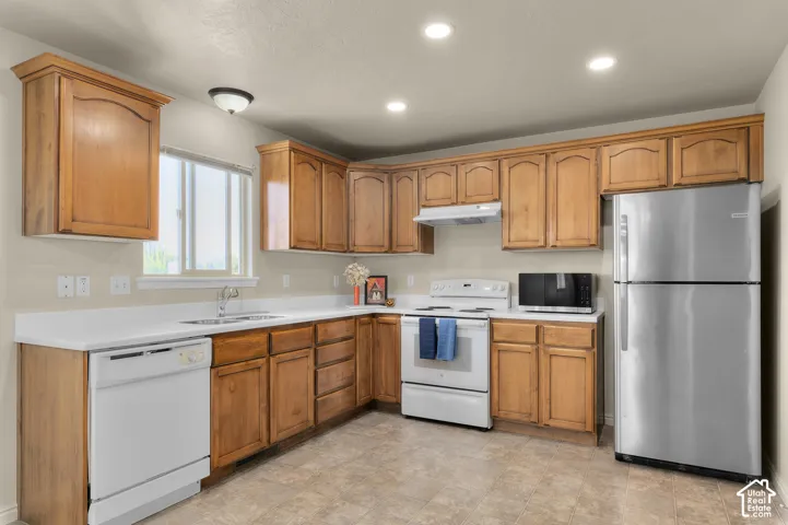 Kitchen featuring wood-finish cabinetry, white countertops, a stainless steel refrigerator, white electric range, and a window above the sink