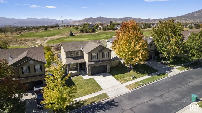 Two-story residence with a two-car garage, front lawn, and mature trees, featuring a golf course backdrop and distant mountains