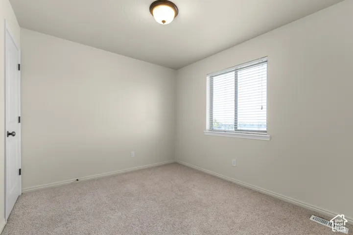 Neutral wall tones, carpeted flooring, a single window with blinds, a white door with black hardware, and a ceiling-mounted light fixture