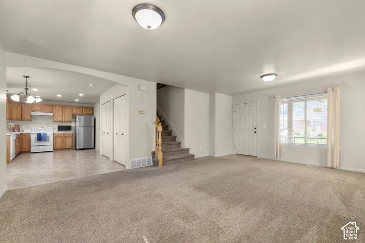 Open-concept living area with carpet flooring, a front entry door, and a multi-pane window