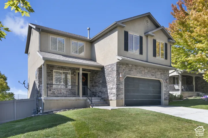 Two-story stucco and stone-faced exterior with an attached garage, covered front porch, and a paved driveway