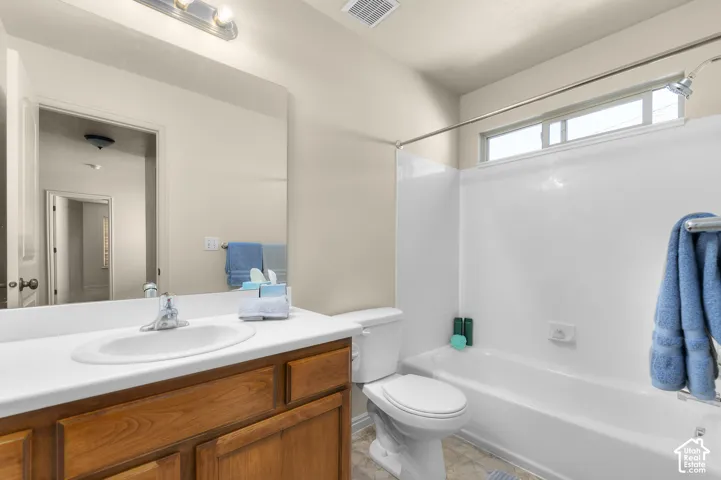 Bathroom featuring a wood-finish vanity with an integrated sink, a large wall-mounted mirror, a full-size bathtub with a shower, and a built-in window