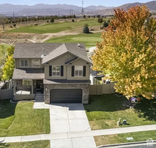 Two-story residence featuring a two-car garage, stone and siding exterior, covered porch, and mature landscaping