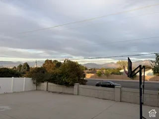 Expansive rooftop deck featuring concrete flooring, perimeter fencing, and mature landscaping with distant mountain vistas framed by natural light and open sky