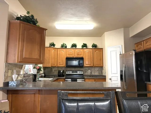 Wood-finish cabinetry, built-in microwave, stainless steel refrigerator, and tiled backsplash