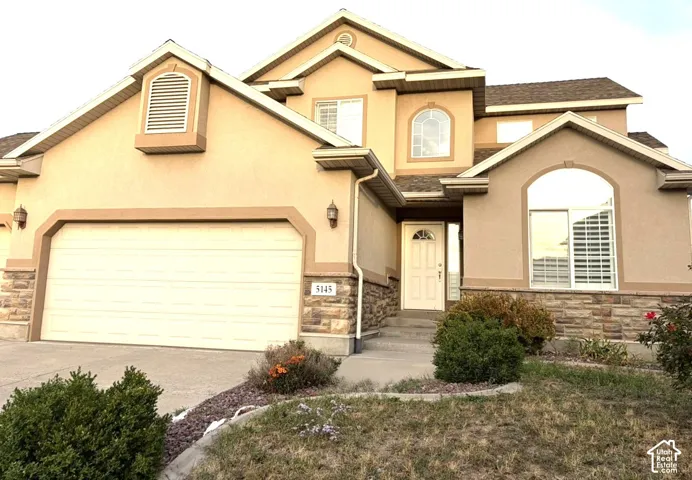 Stucco exterior with stone accents, arched windows, an attached garage, and a front entry door with sidelights