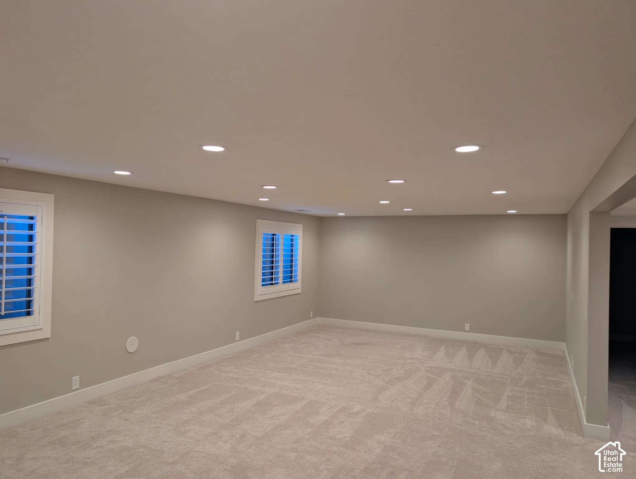 Recessed lighting, neutral wall tones, two windows with white plantation shutters, and light-toned carpet flooring