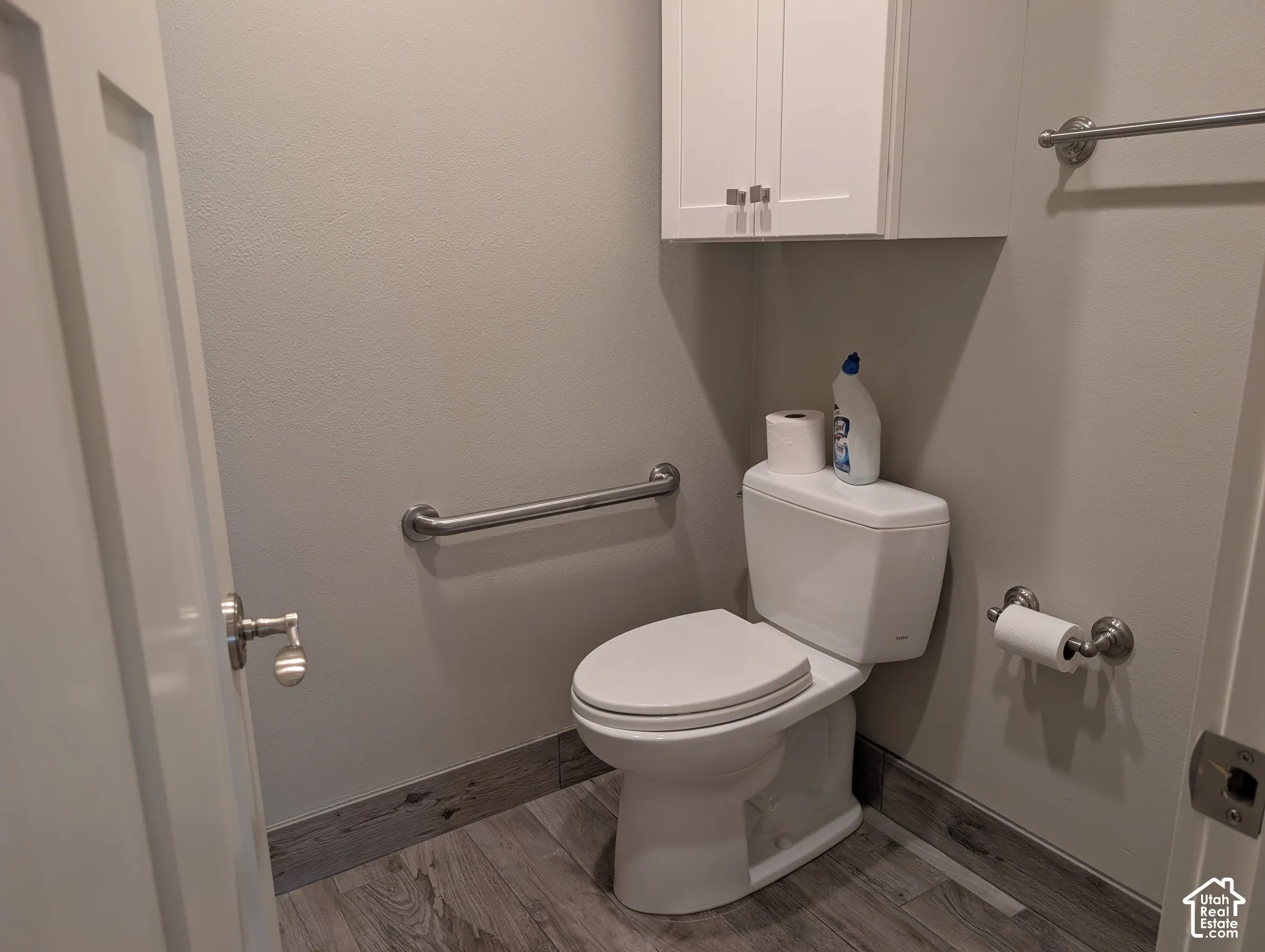 Wood-finish flooring, wall-mounted cabinetry, white toilet, and brushed nickel hardware