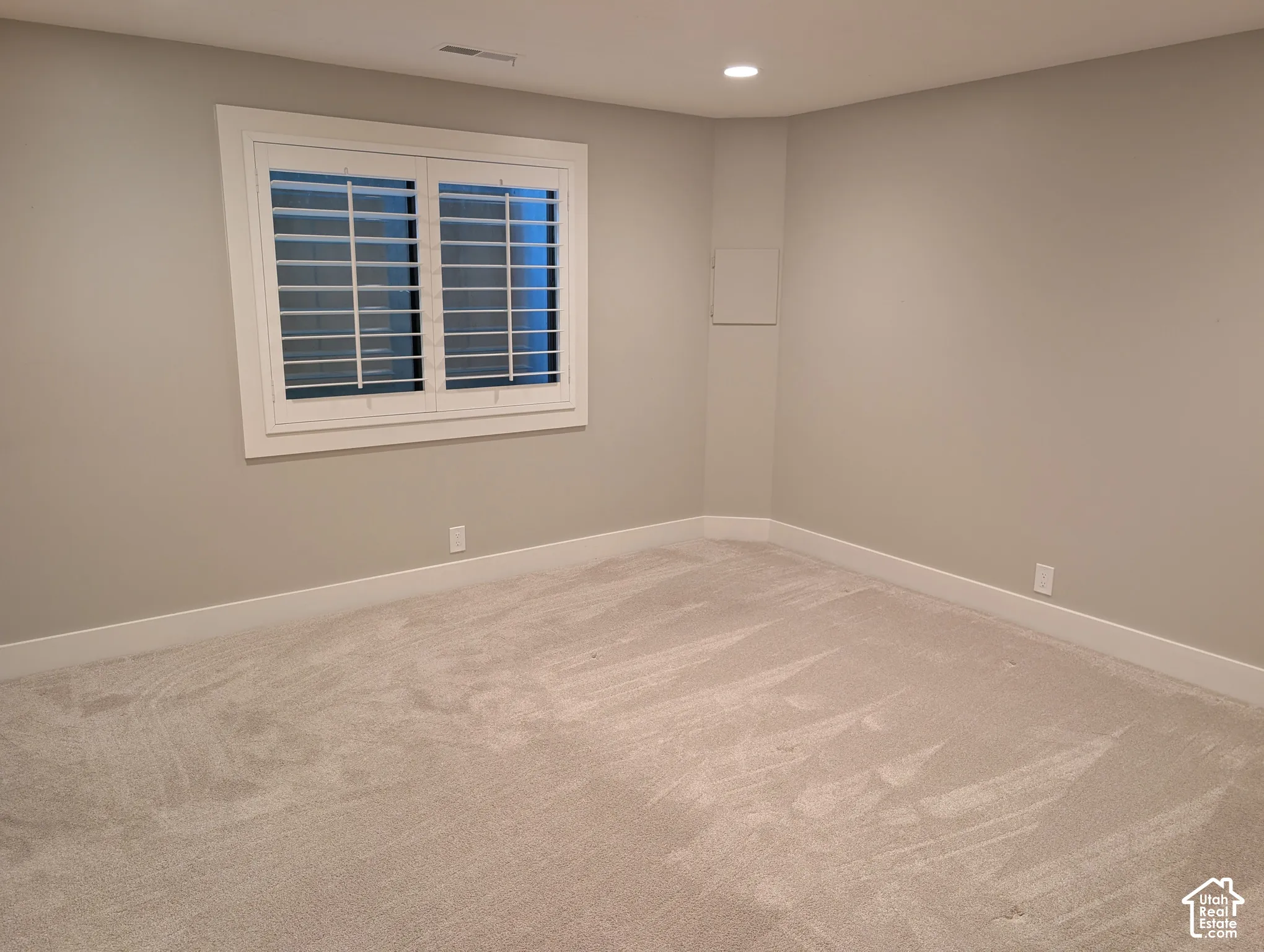 Window with white plantation shutters, recessed ceiling lighting, light-toned wall paint, white trim, and light-colored carpet flooring
