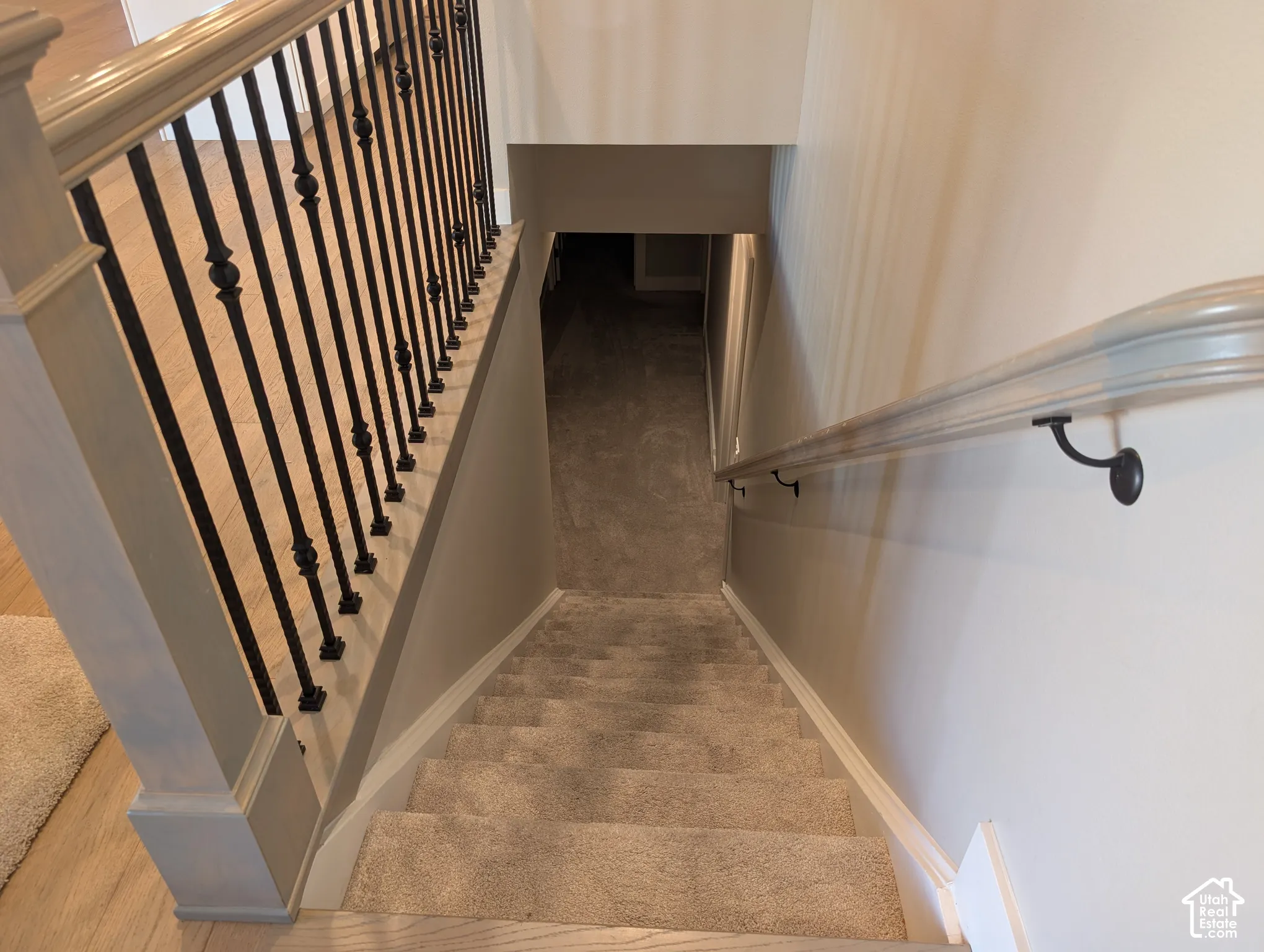 Carpeted staircase with light wood-finish handrail, wrought iron balusters, and white baseboards