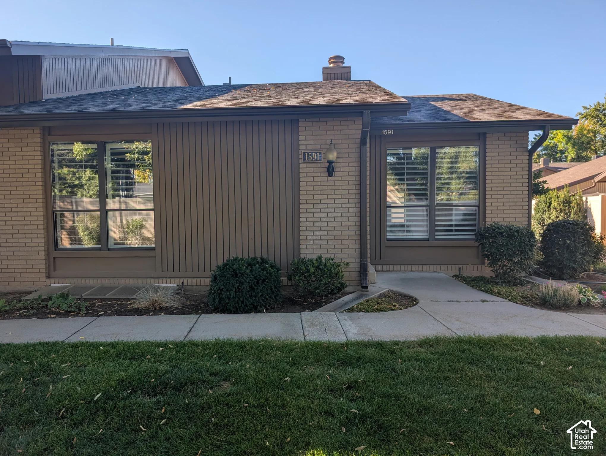 Brick and vertical siding exterior with contrasting trim, featuring multiple windows, a prominent entry light fixture, and a concrete walkway
