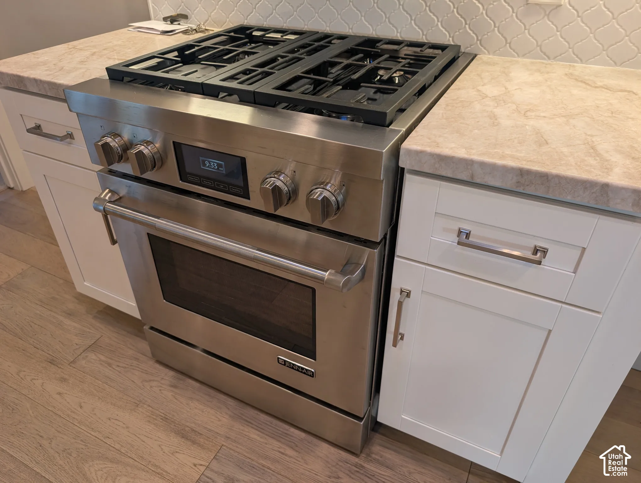 Stainless steel range with a gas cooktop, light-toned countertops, white shaker-style cabinetry, and wood-finish flooring